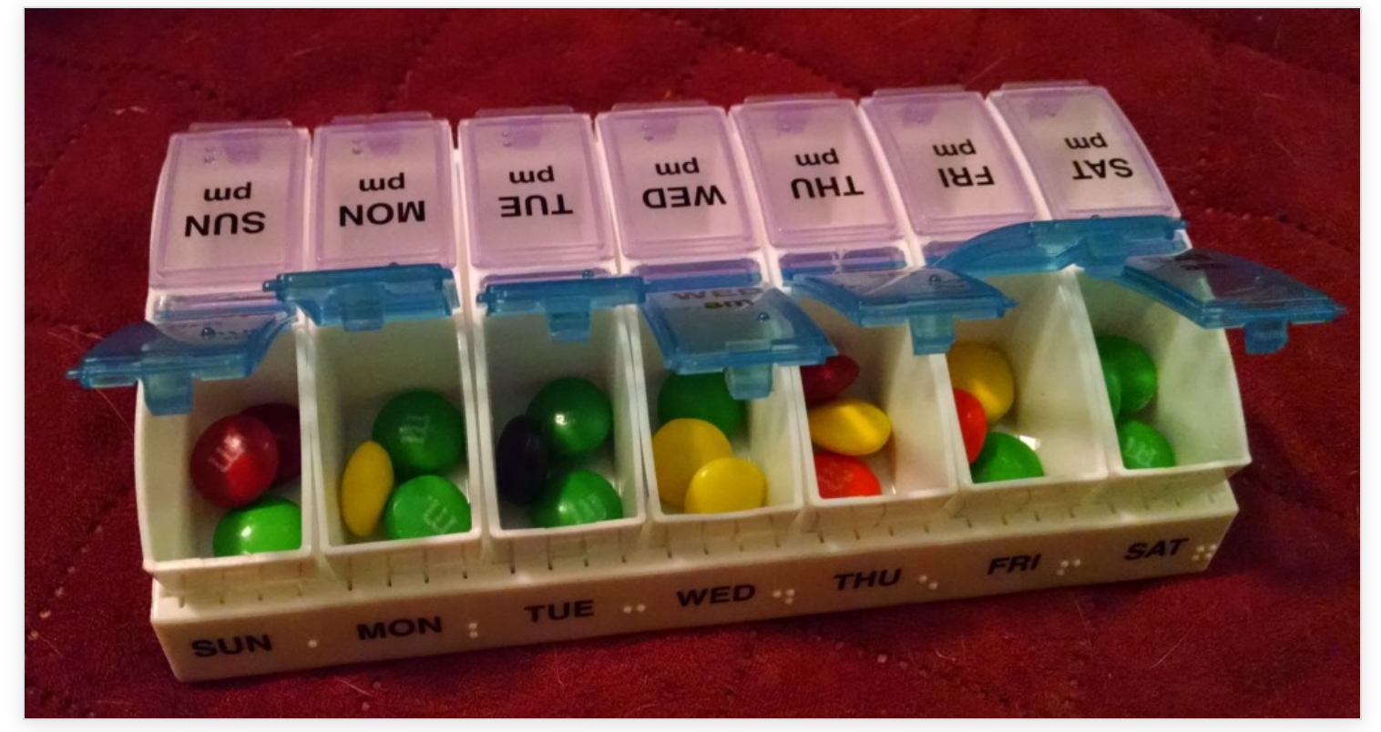 A weekly pill organizer filled with colorful candies