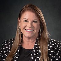 A woman is wearing a black and white polka dot jacket and smiling.