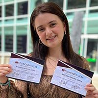 A woman is holding two certificates in front of a building.