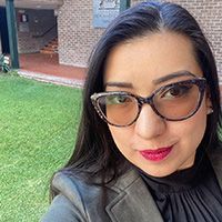 A woman wearing glasses is taking a selfie in front of a brick building.
