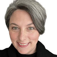 A woman with gray hair is smiling and wearing a black sweater.