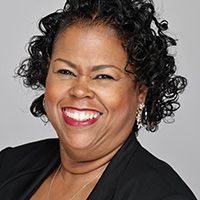 A woman with curly hair is smiling and wearing a black jacket.