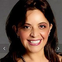 A woman is smiling and wearing a necklace and earrings.