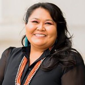 A woman wearing a black shirt and a necklace is smiling for the camera.