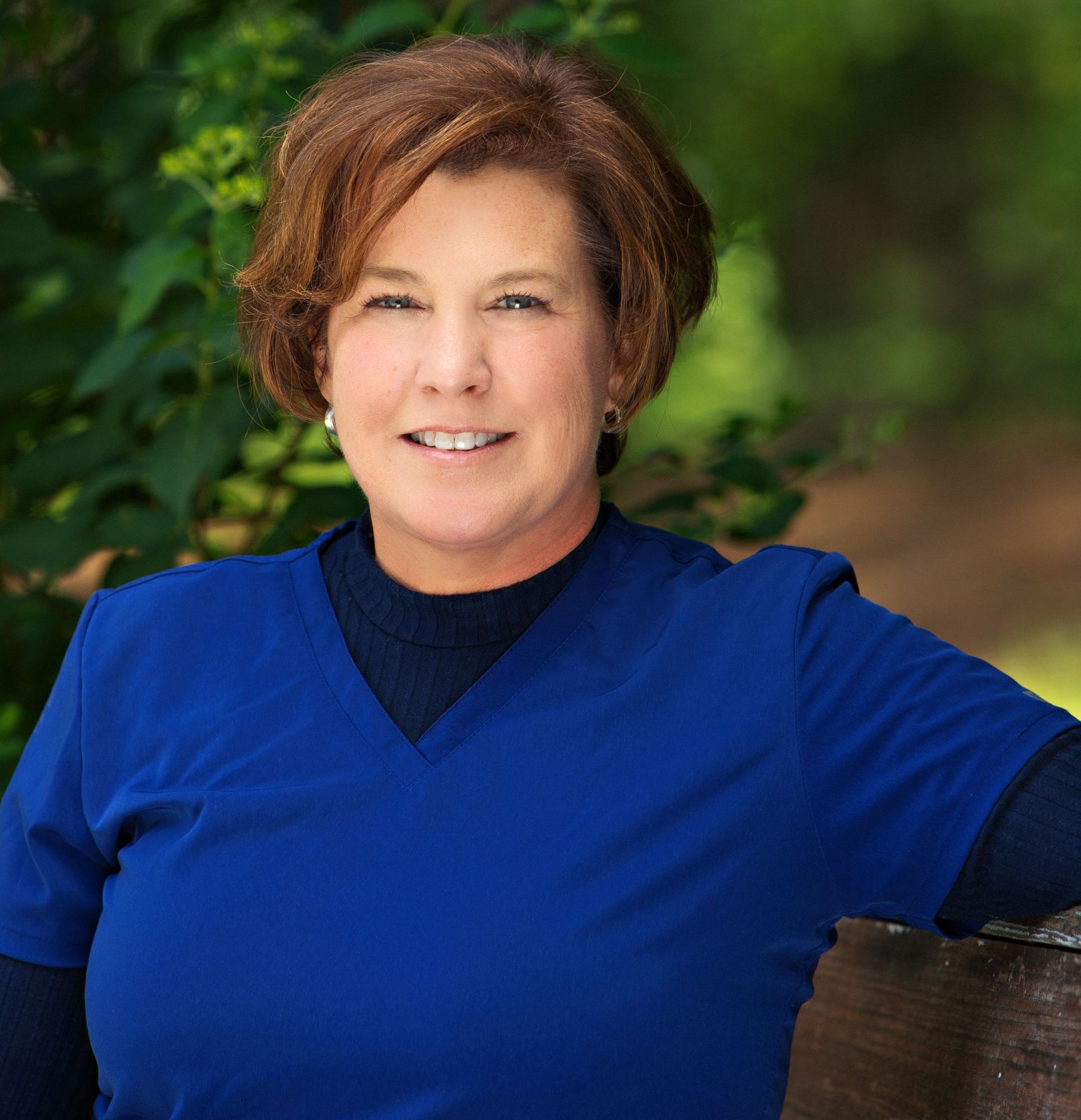 A woman in a blue scrub top is sitting on a bench.