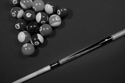 Billiard balls racked on a pool table beside a cue stick