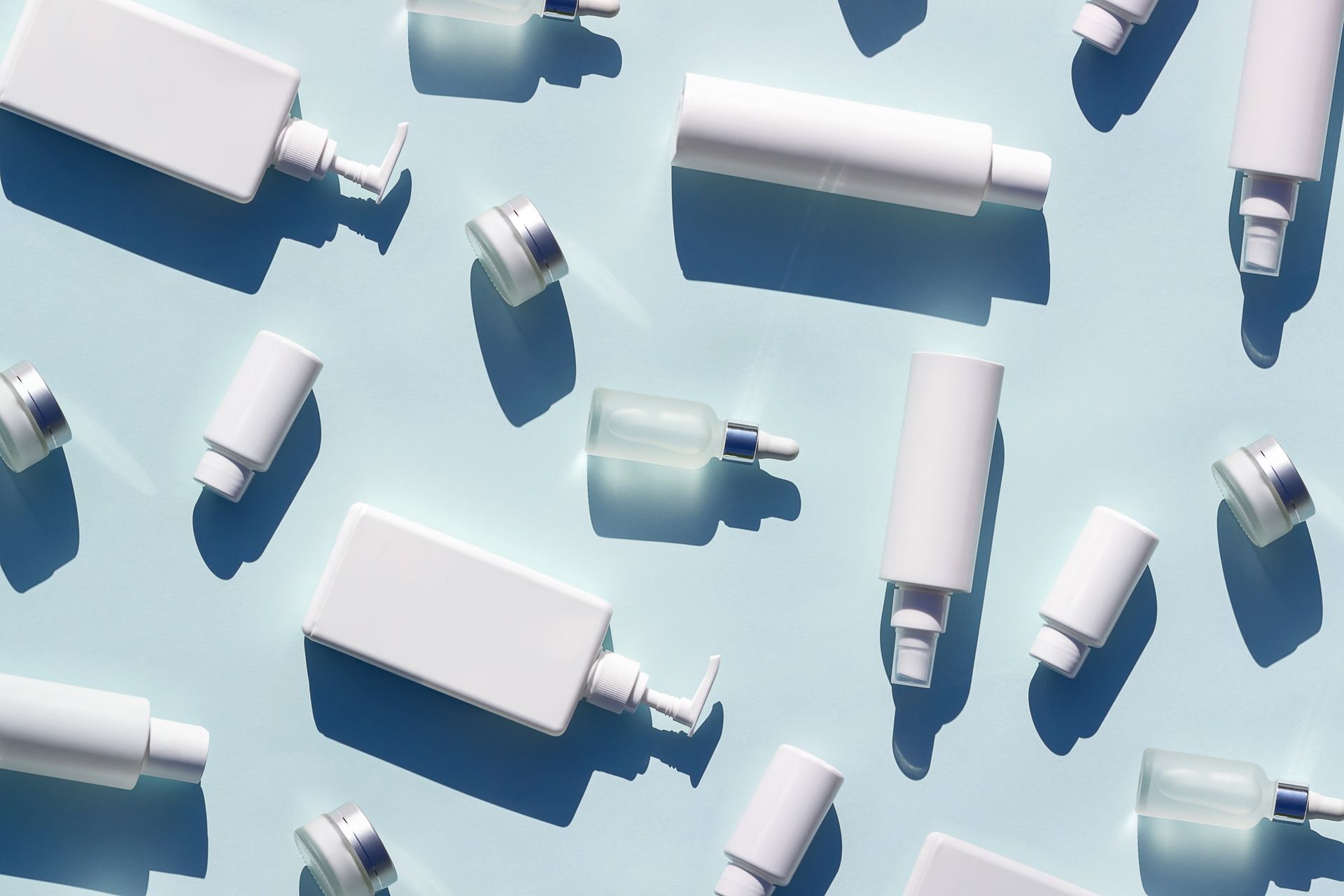 White cosmetic bottles, tubes and jars laid flat on a blue background as packaging products.