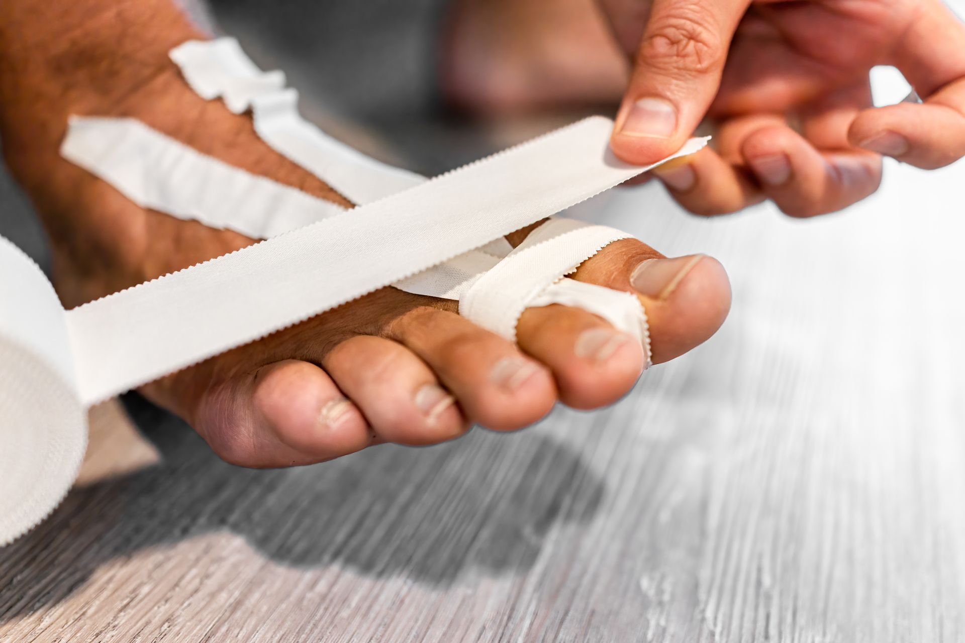 Person wrapping white bandage around foot and toes.