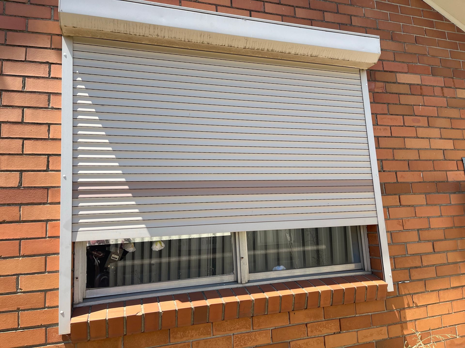 White window roller shutter partly closed on a brick building exterior.