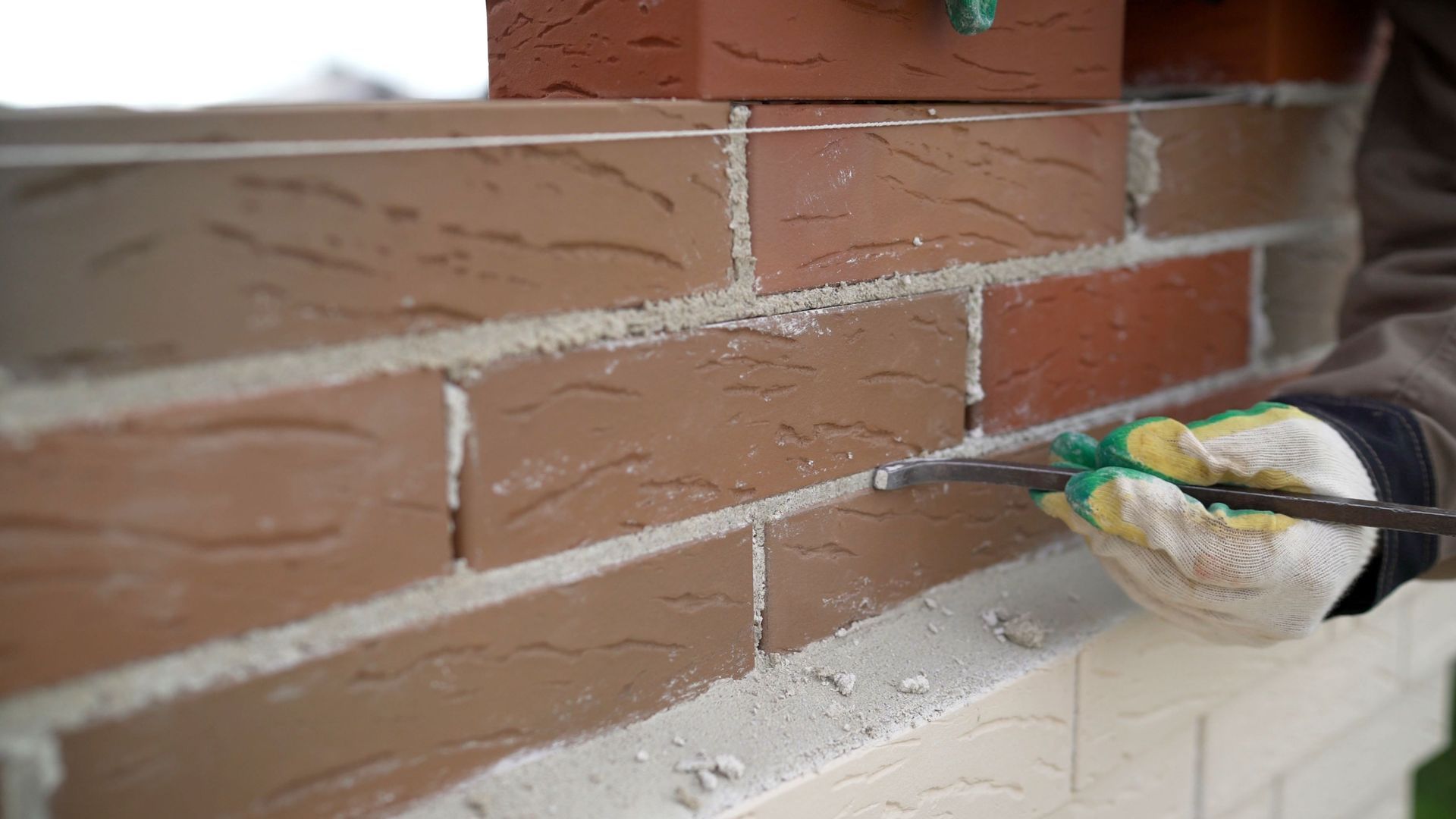 A duck with green head and yellow beak perched on a brick ledge beside a wall.