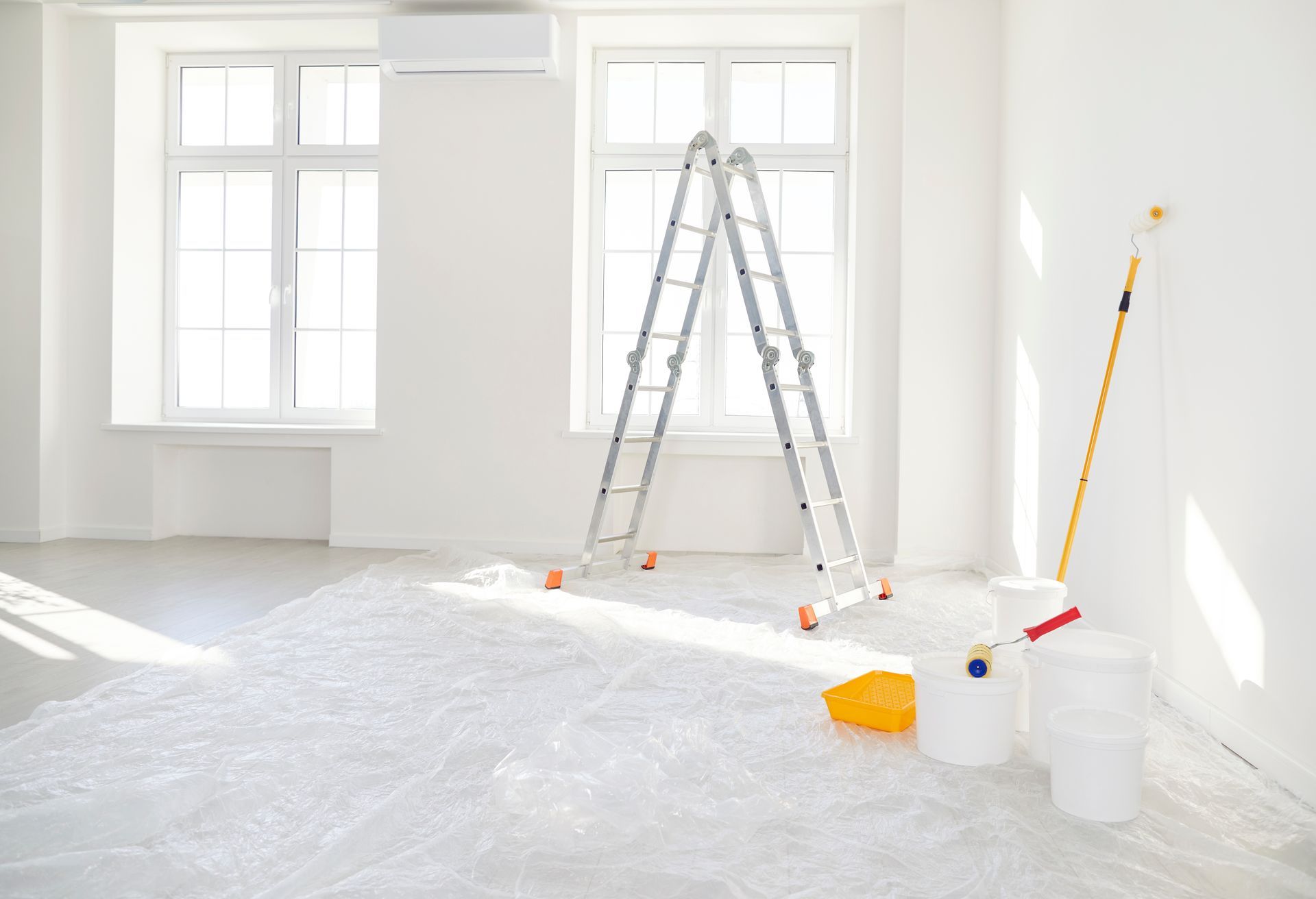 Bright white room under renovation with ladder, paint cans, drop cloth, and tools near windows