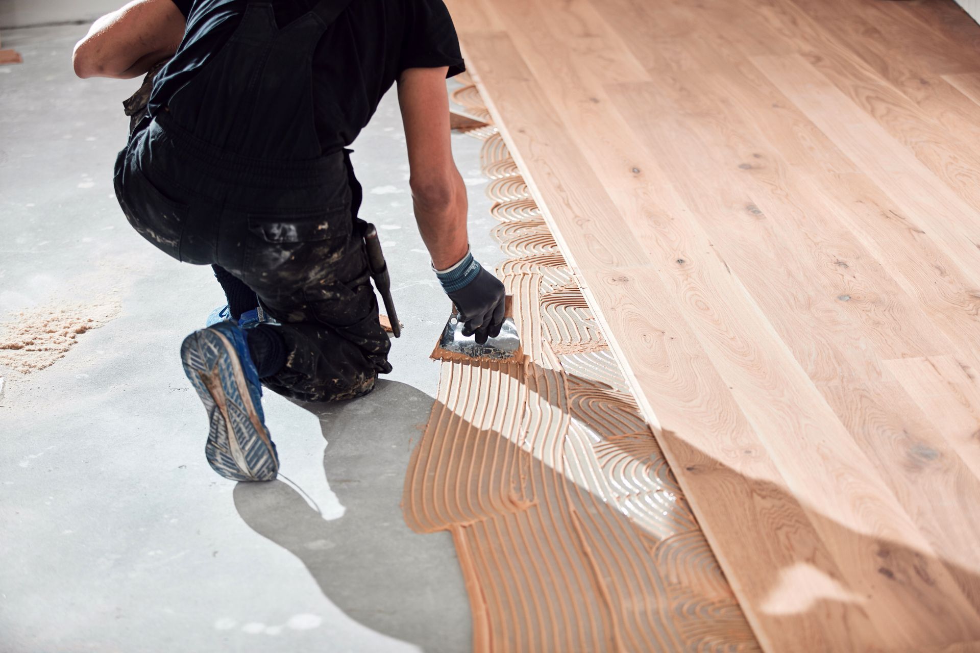 Worker kneeling and spreading adhesive on a wooden floor during installation