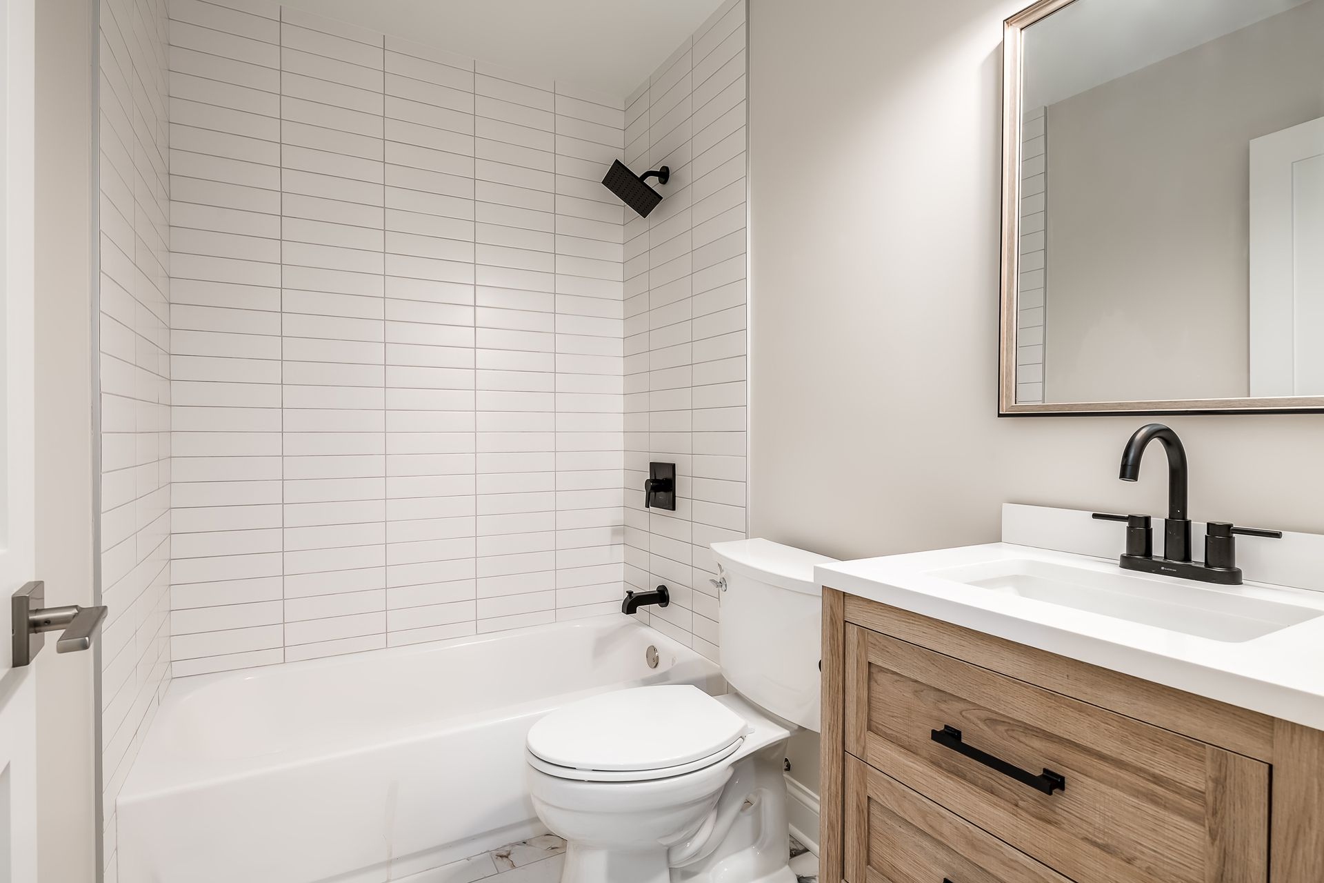 Modern white bathroom with bathtub, toilet, wood vanity, and black fixtures