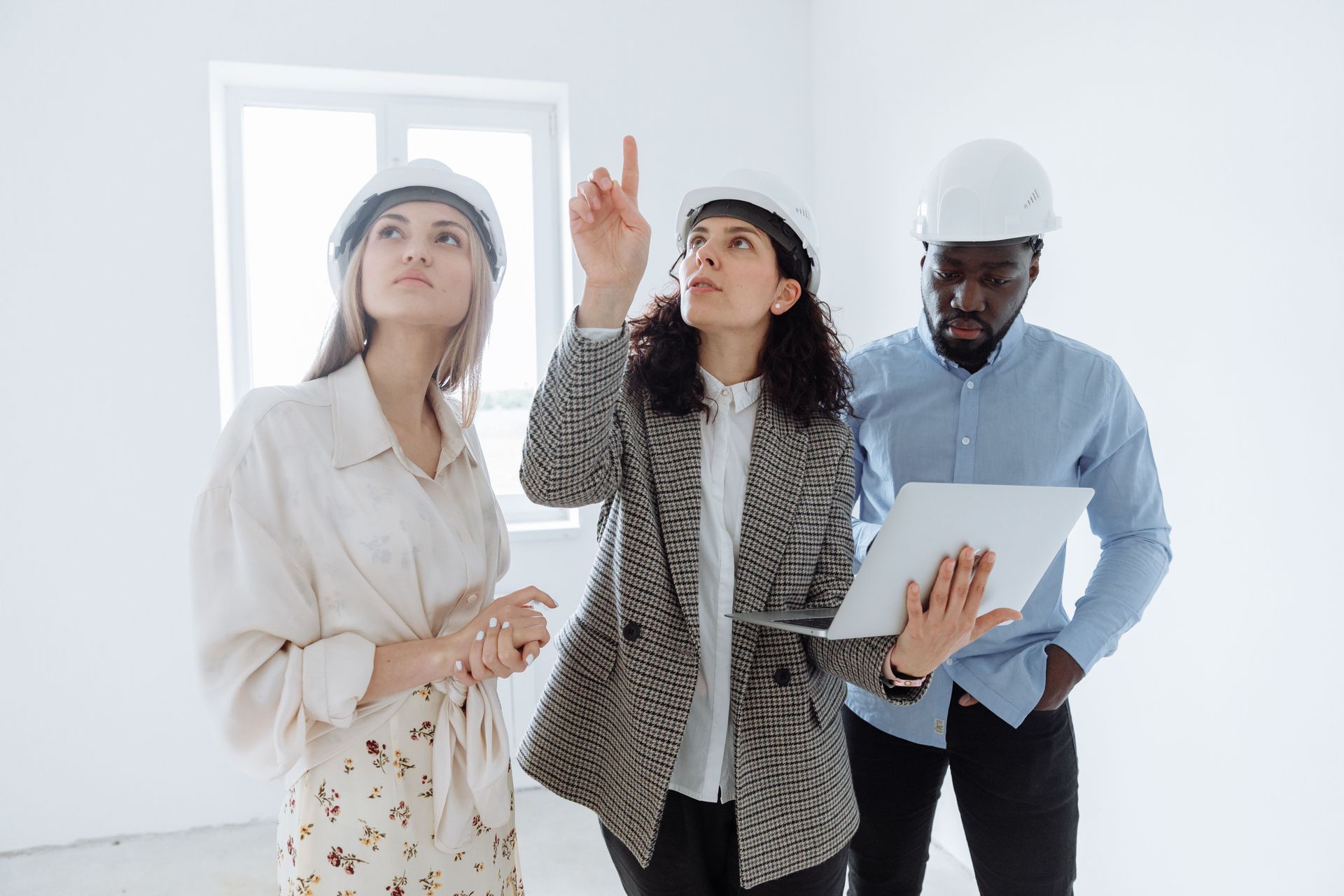 Two electricians in hard hats inspect exposed wiring in a bright room.
