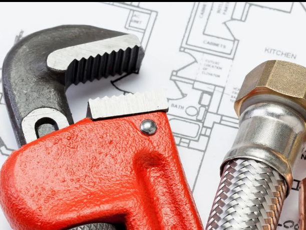 Plumber under a sink repairing pipes with tools and fittings on the floor