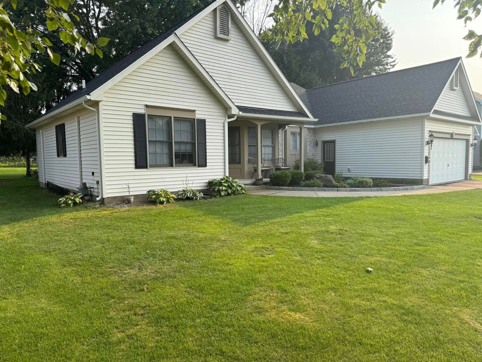 White house with black shutters and attached garage, green lawn.