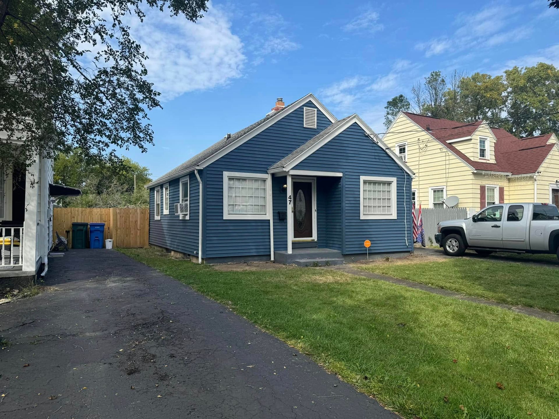 Blue house with white trim and a black driveway under a blue sky.