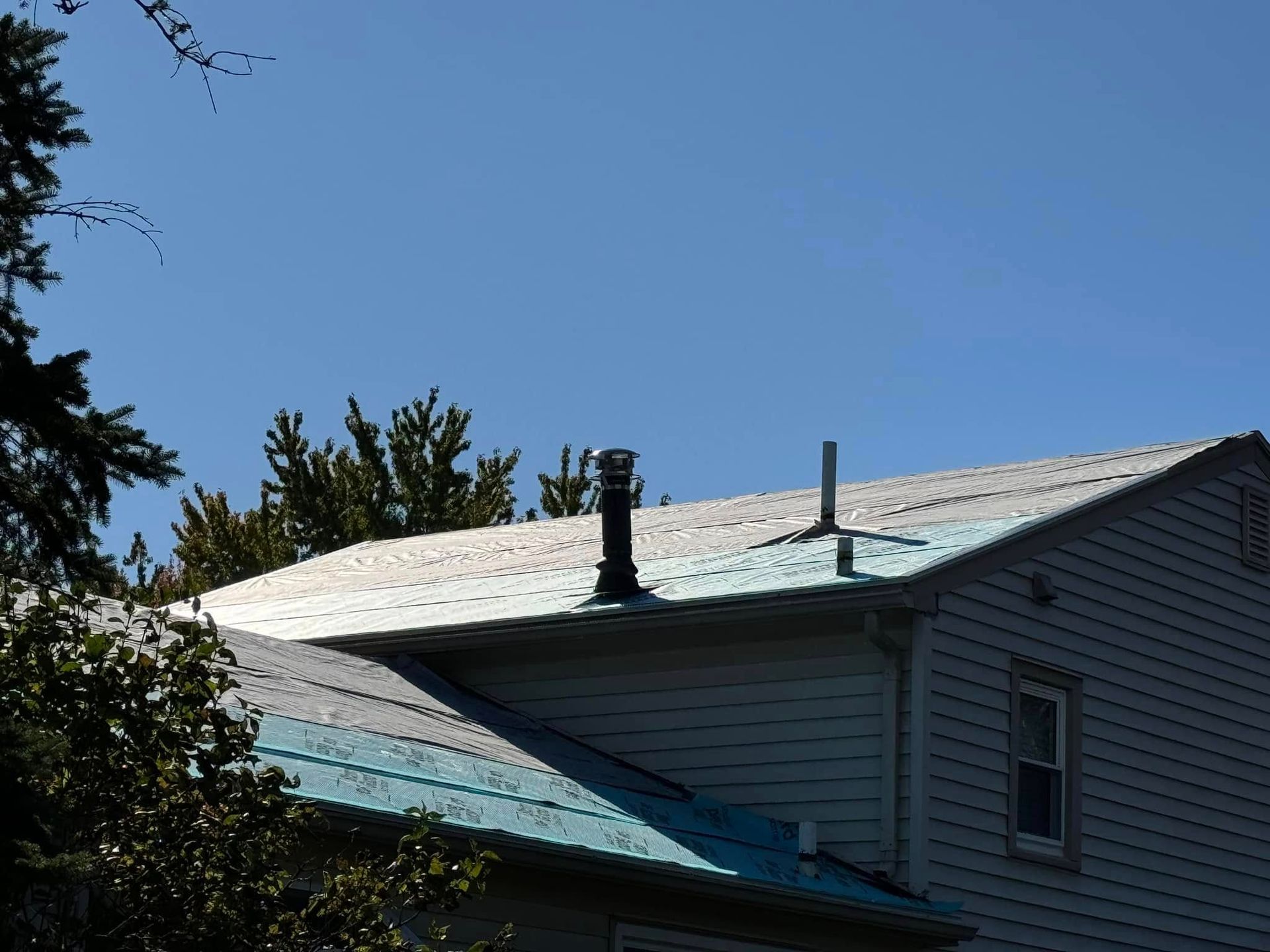 Metal roof of a house with a chimney and pipe against a blue sky.