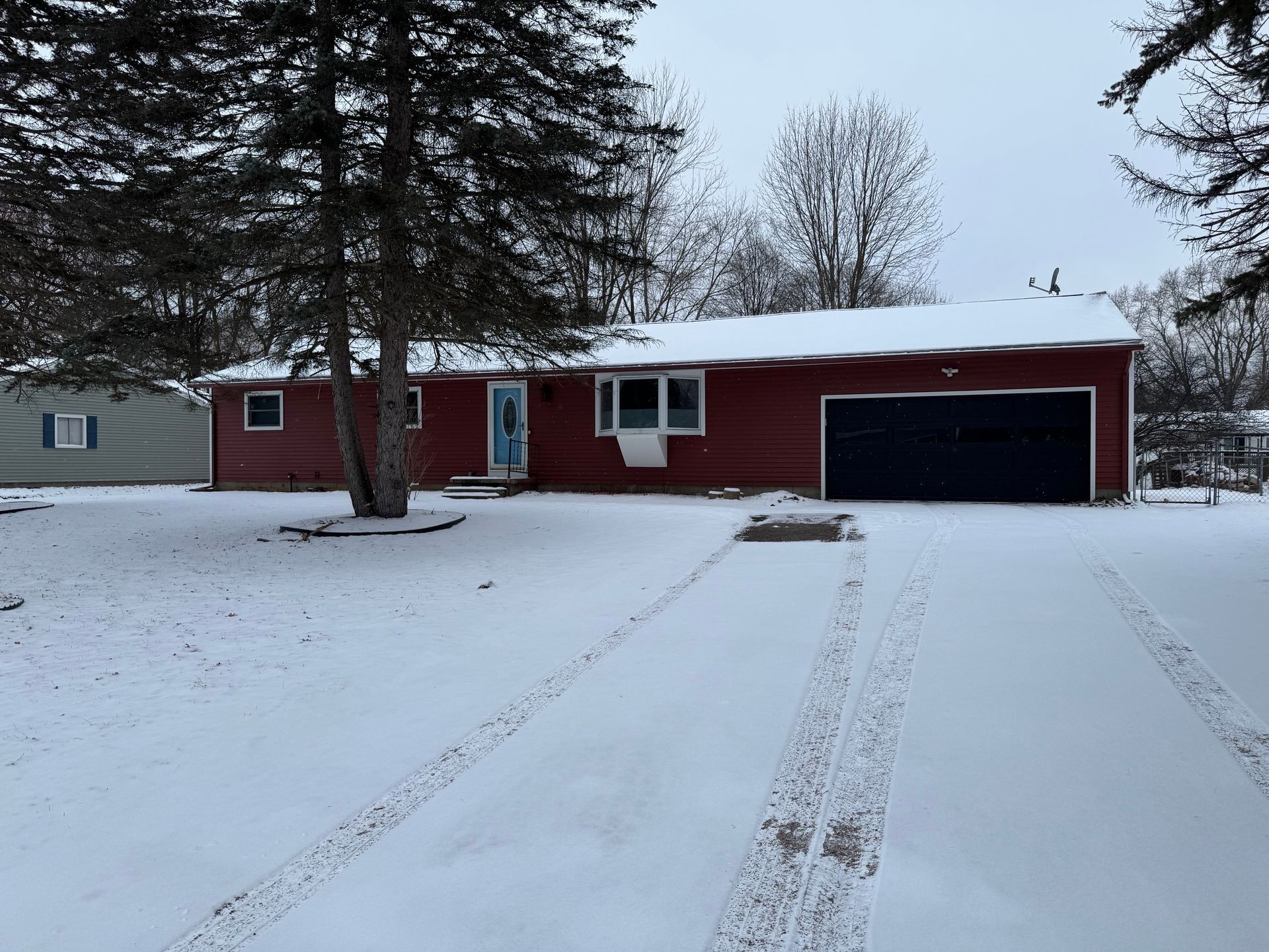 Red house covered in snow; driveway with tire tracks; cloudy winter day.