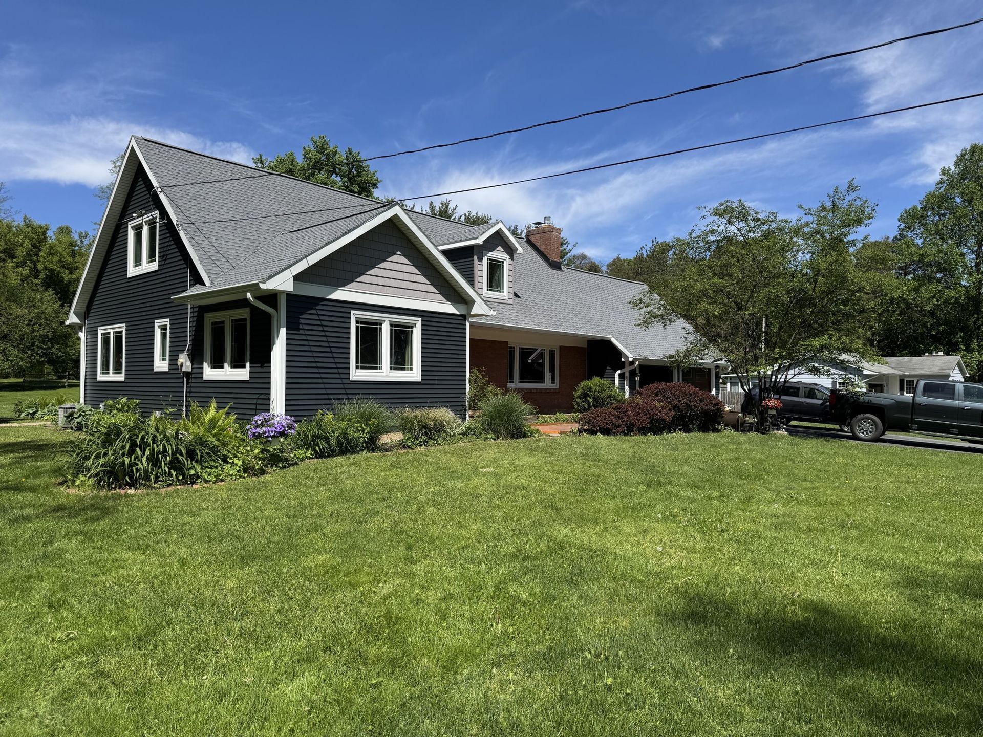 Black and gray house with white trim, green lawn, blue sky, and a truck parked in the yard.