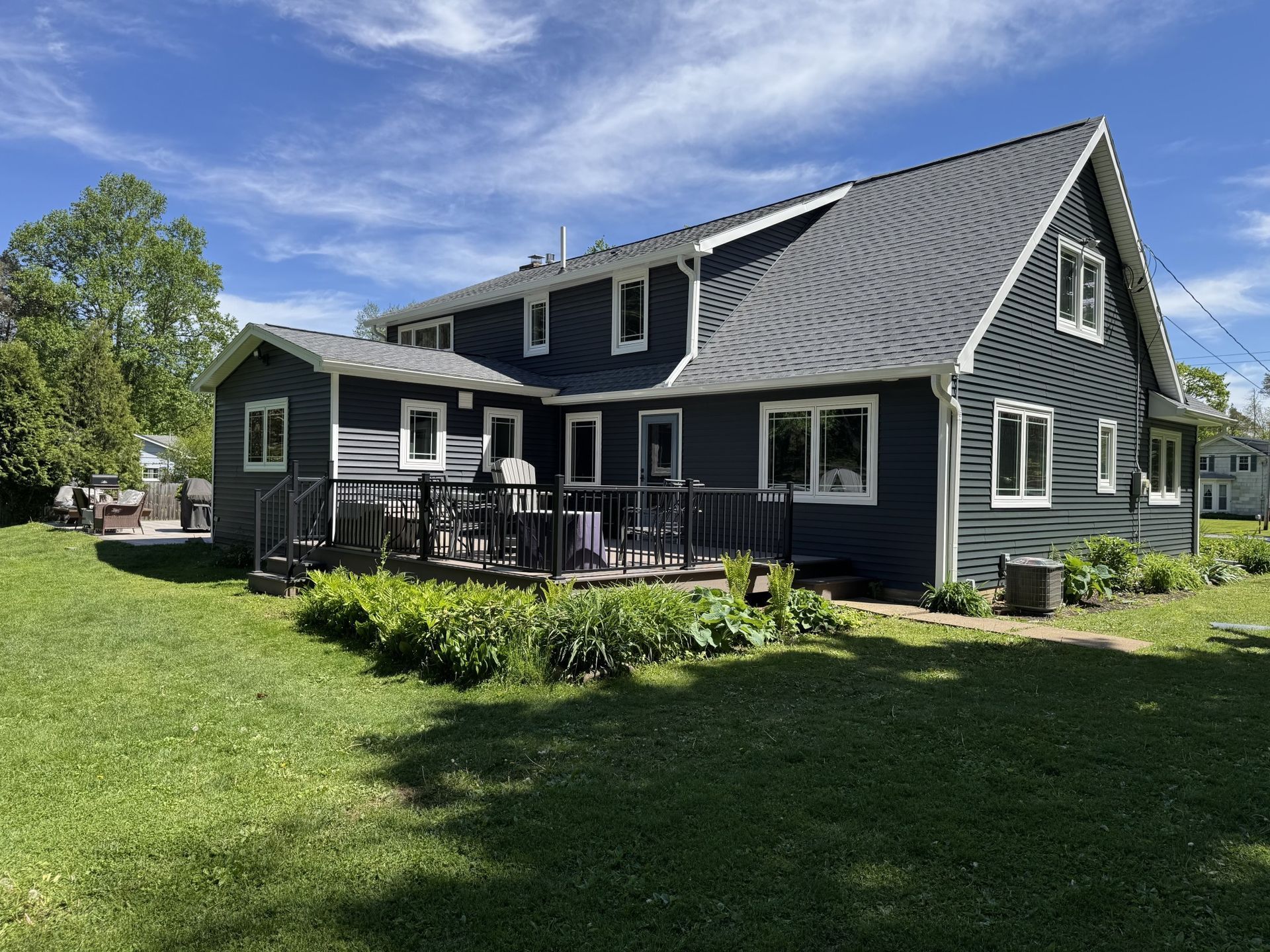 Blue house with deck and black railings, green grass, sunny day.