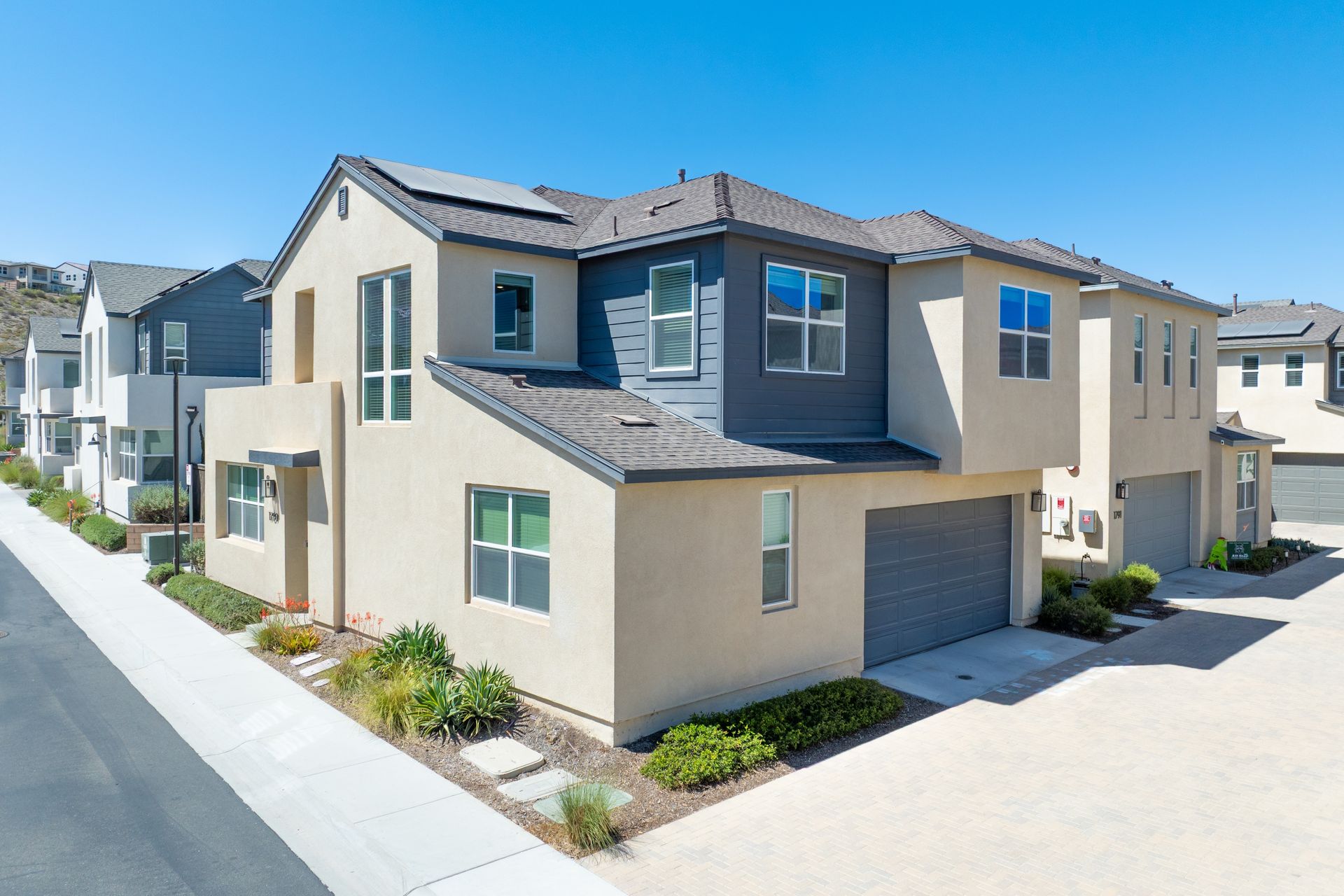 Modern two-story townhomes with light tan and gray exteriors under a clear blue sky.