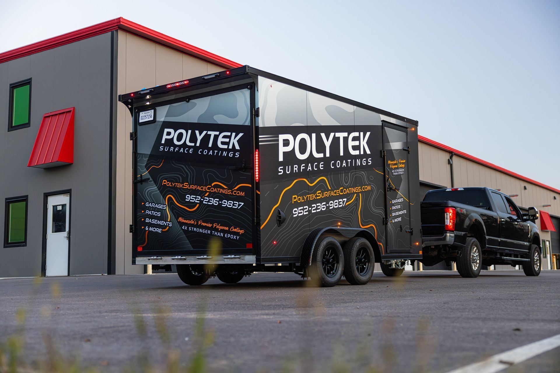 A black truck is towing a black trailer in front of a building.