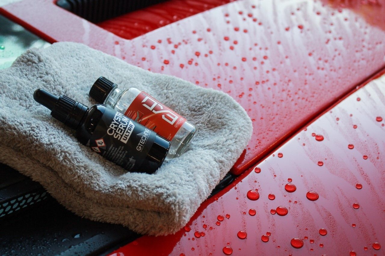 Two bottles of polish are sitting on a towel on the hood of a red car. Two bottles of polish are sitting on a towel on the hood of a red car.