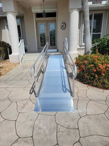 Blue wheelchair ramp leading to a home’s front door, with railings and stone walkway