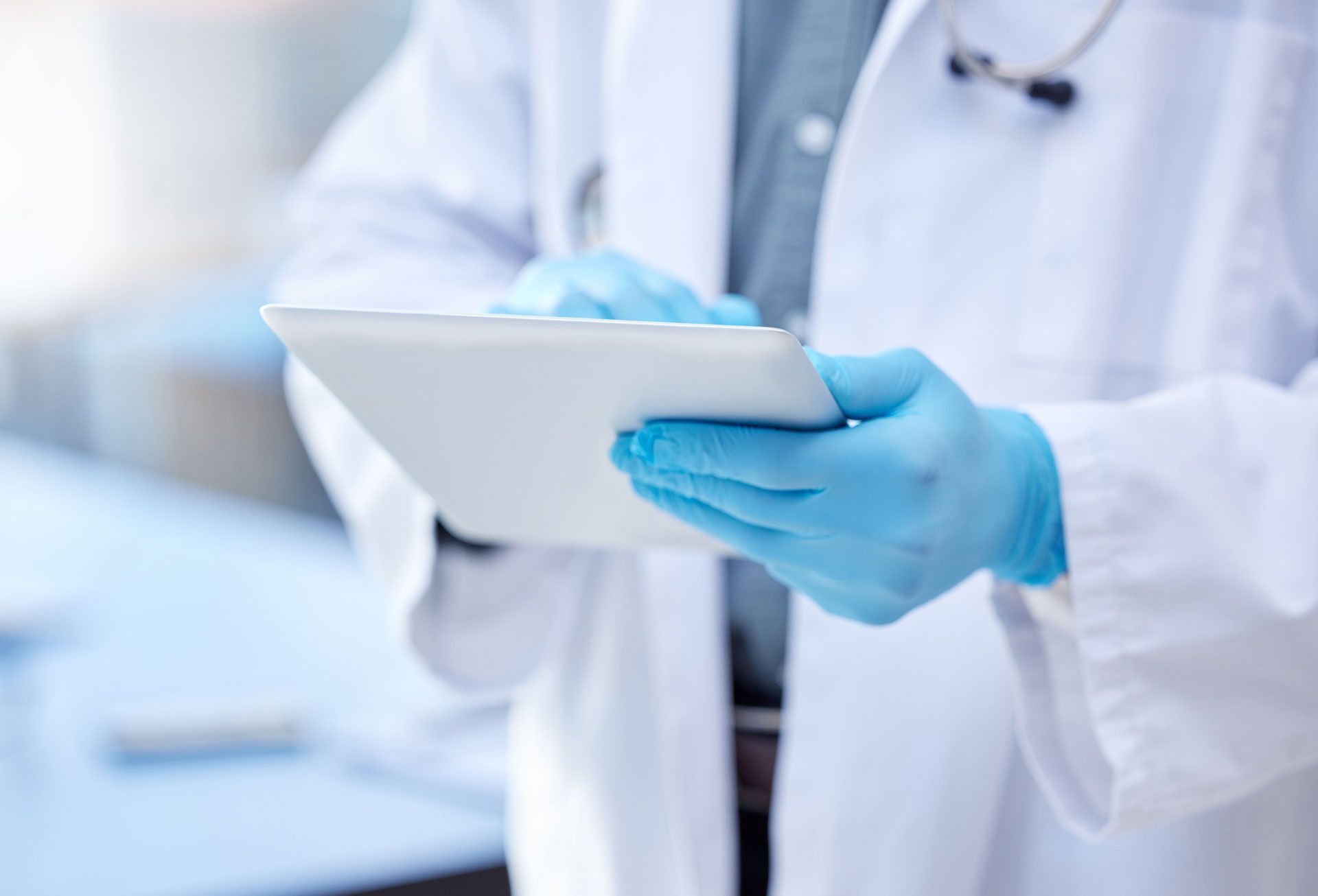 Doctor in white coat wearing blue gloves using a tablet in a medical setting