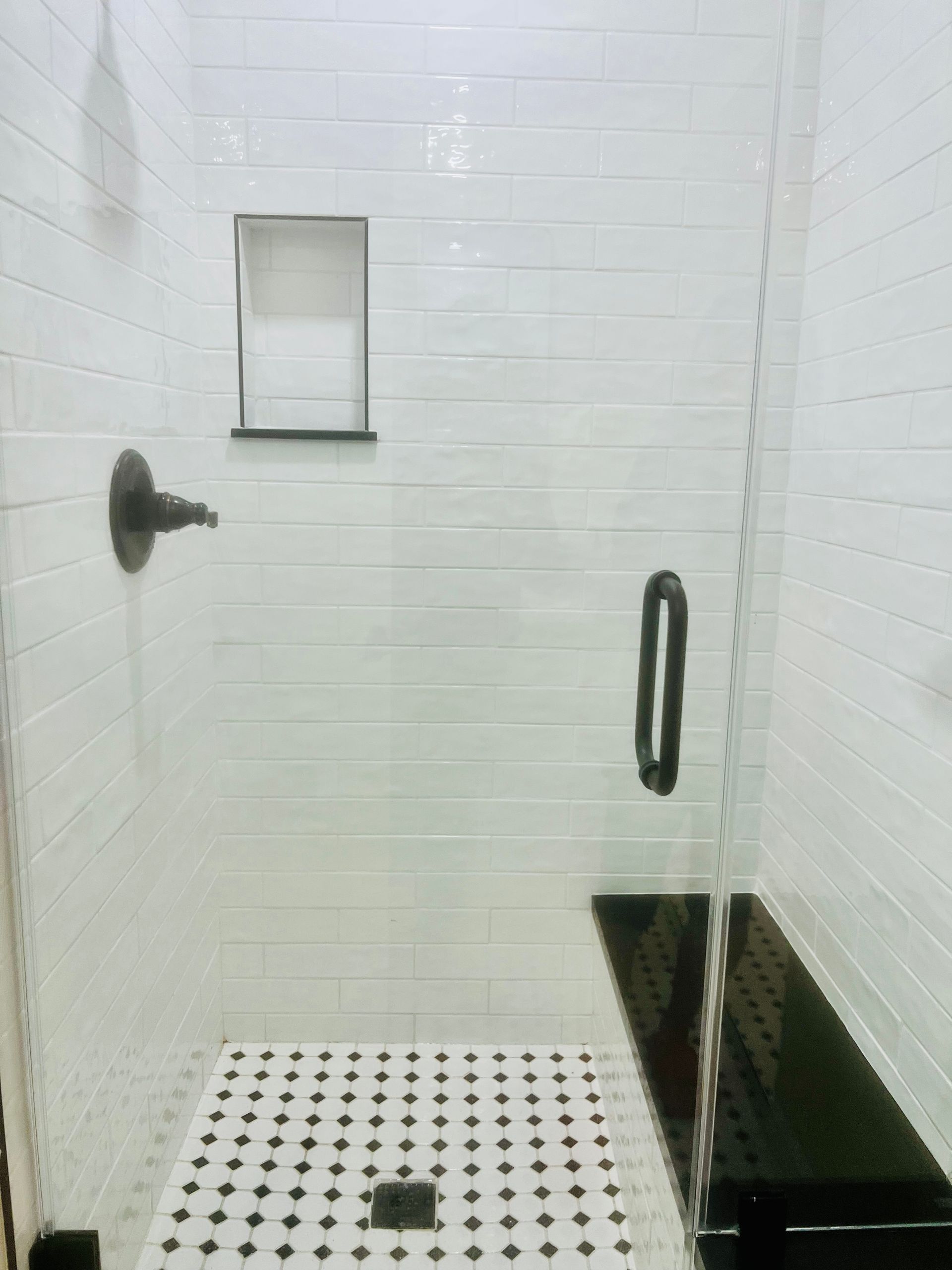White tiled shower with black accents, including a bench and floor pattern.