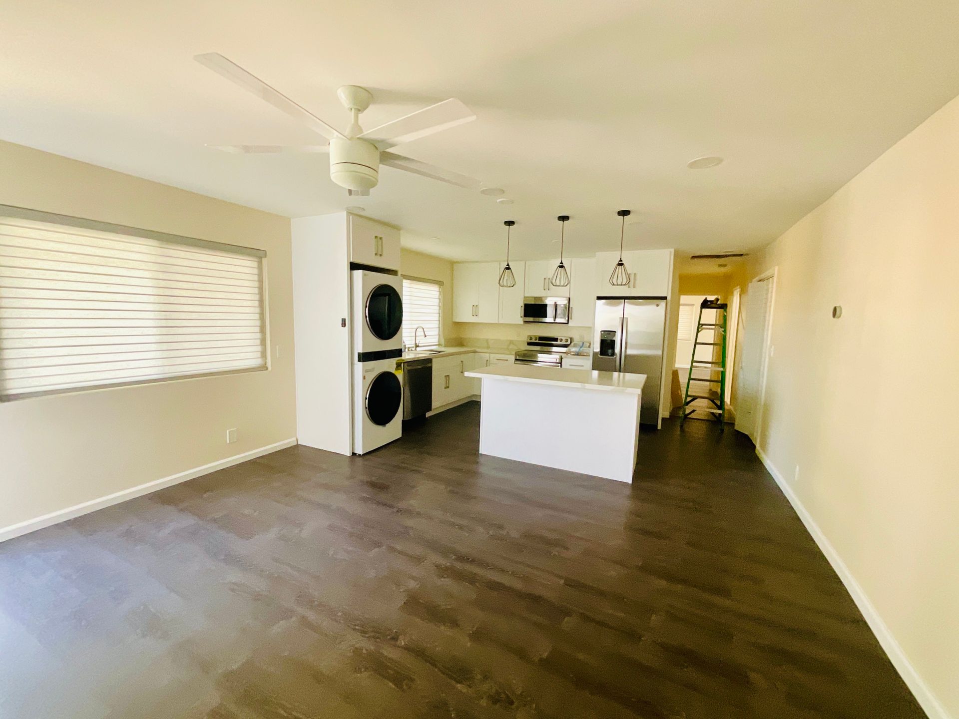 Open-concept kitchen with white cabinets, island, and appliances. Dark wood flooring and a ceiling fan.