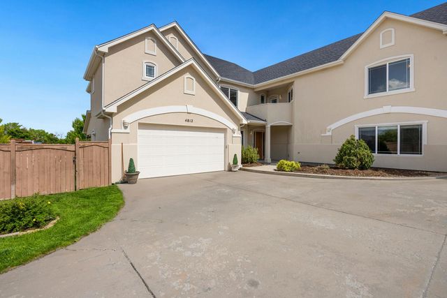 Two-story beige house with a white garage door, driveway, and a wooden fence under a blue sky.