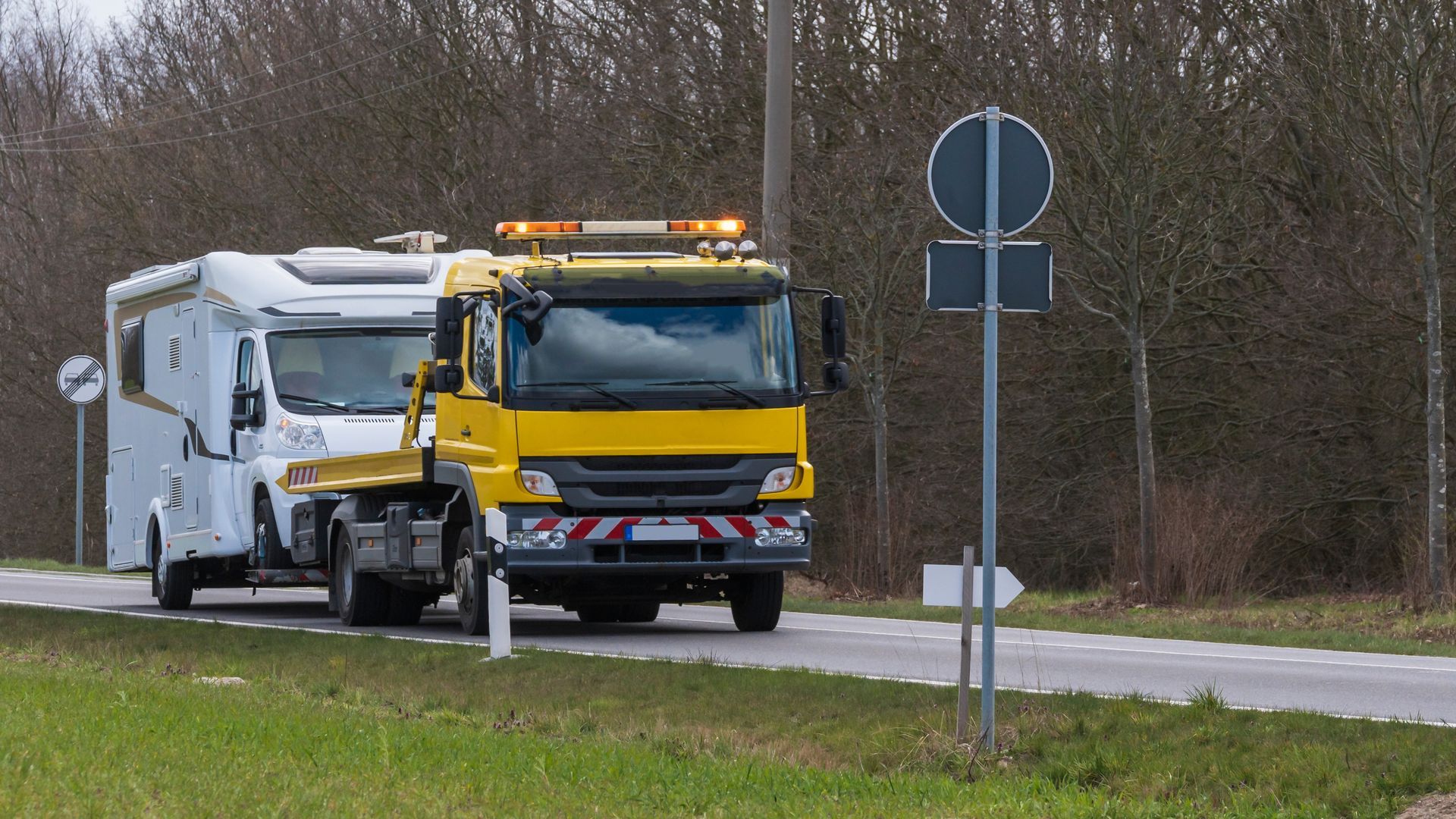 A professional yellow flatbed truck providing specialized RV towing for a white motorhome.
