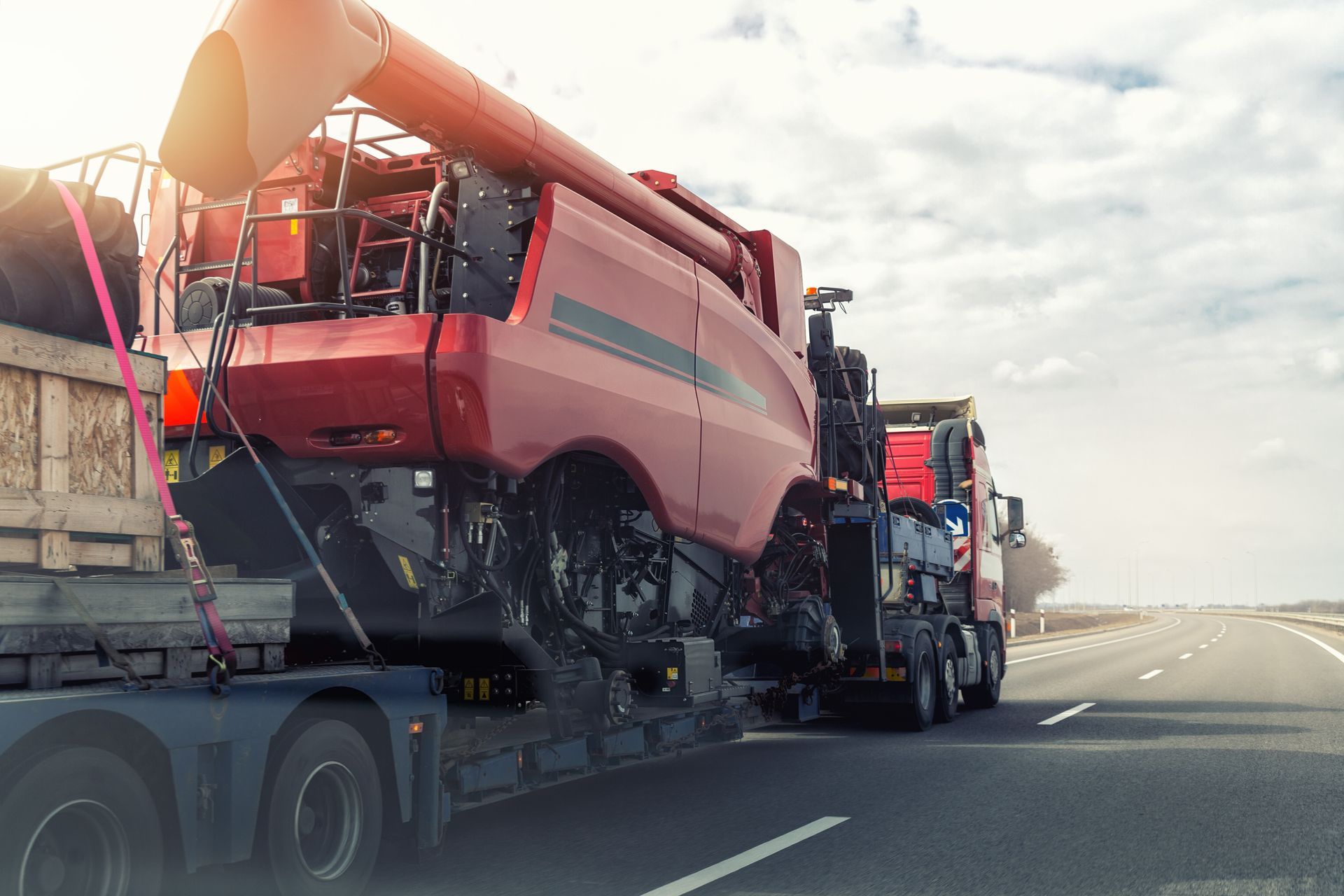 A red combine harvester is being transported on a flatbed trailer on a highway.