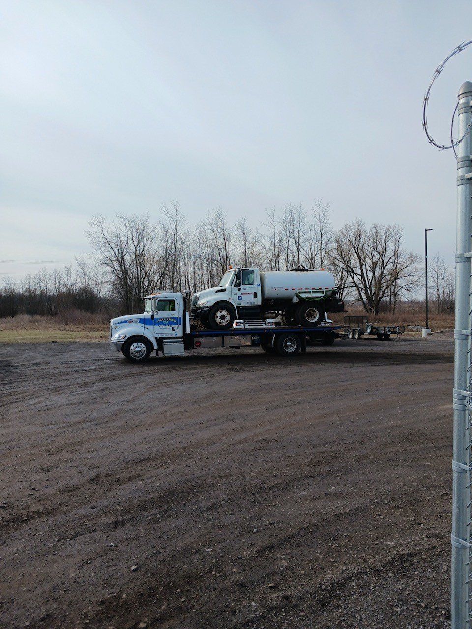 Flatbed tow truck hauling a pickup truck across a gravel lot