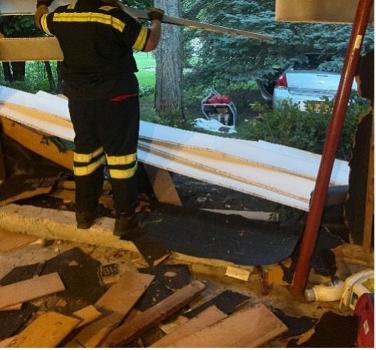 Firefighter standing by a broken window with debris inside a damaged building.
