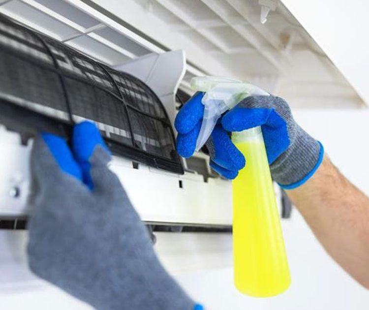 A person is cleaning an air conditioner with a spray bottle.