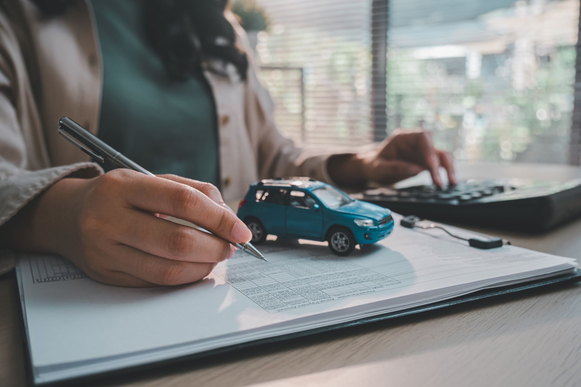 A hand holding a pen over an insurance policy next to a toy car and calculator on a desk