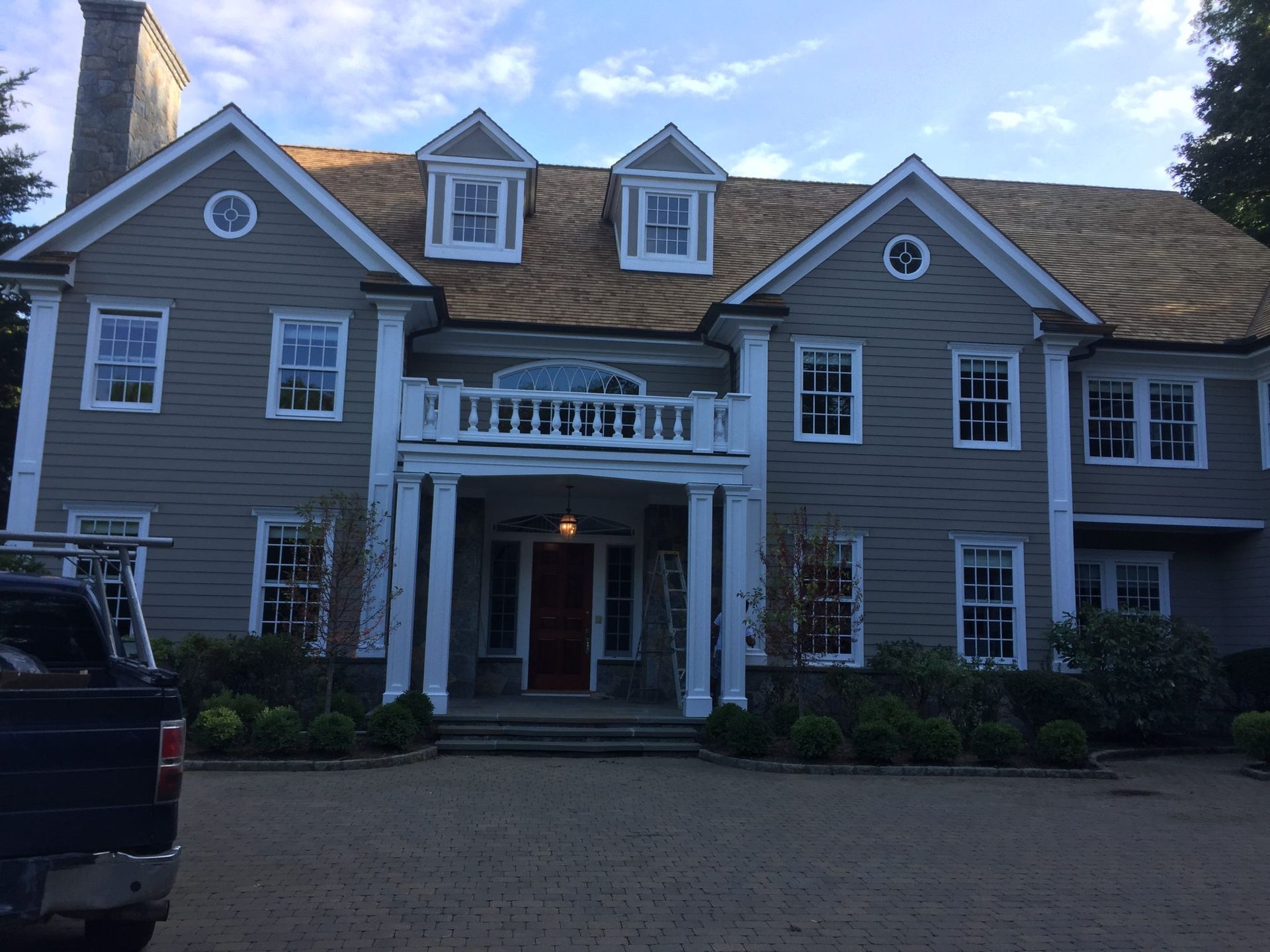 A large, two-story house with gray siding, a white pillared entrance, two dormer windows, and a newly shingled roof.