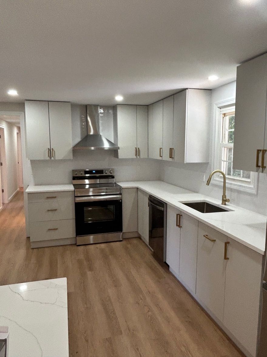 A modern kitchen featuring white cabinets, quartz countertops, stainless steel appliances, and wood-look flooring.