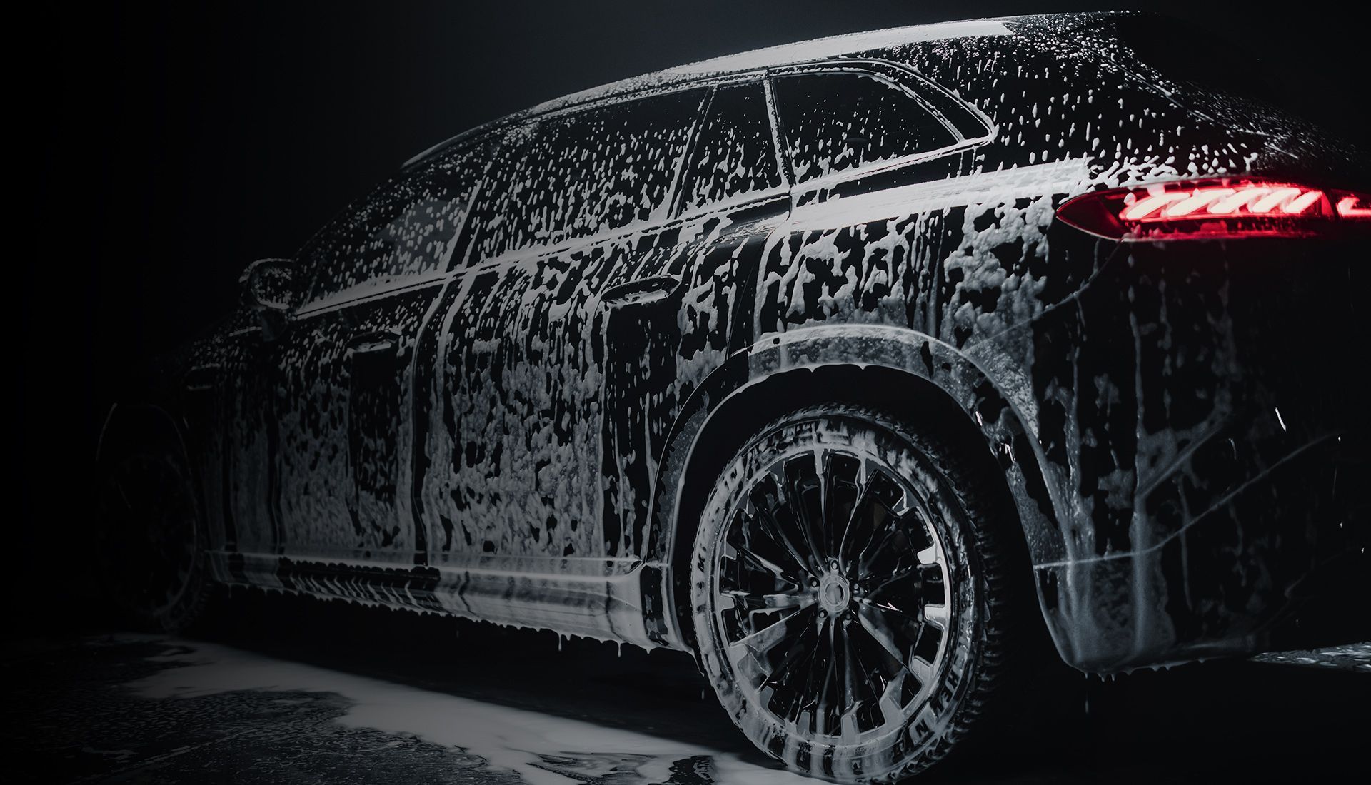 Black SUV covered in soap suds, illuminated in the dark.