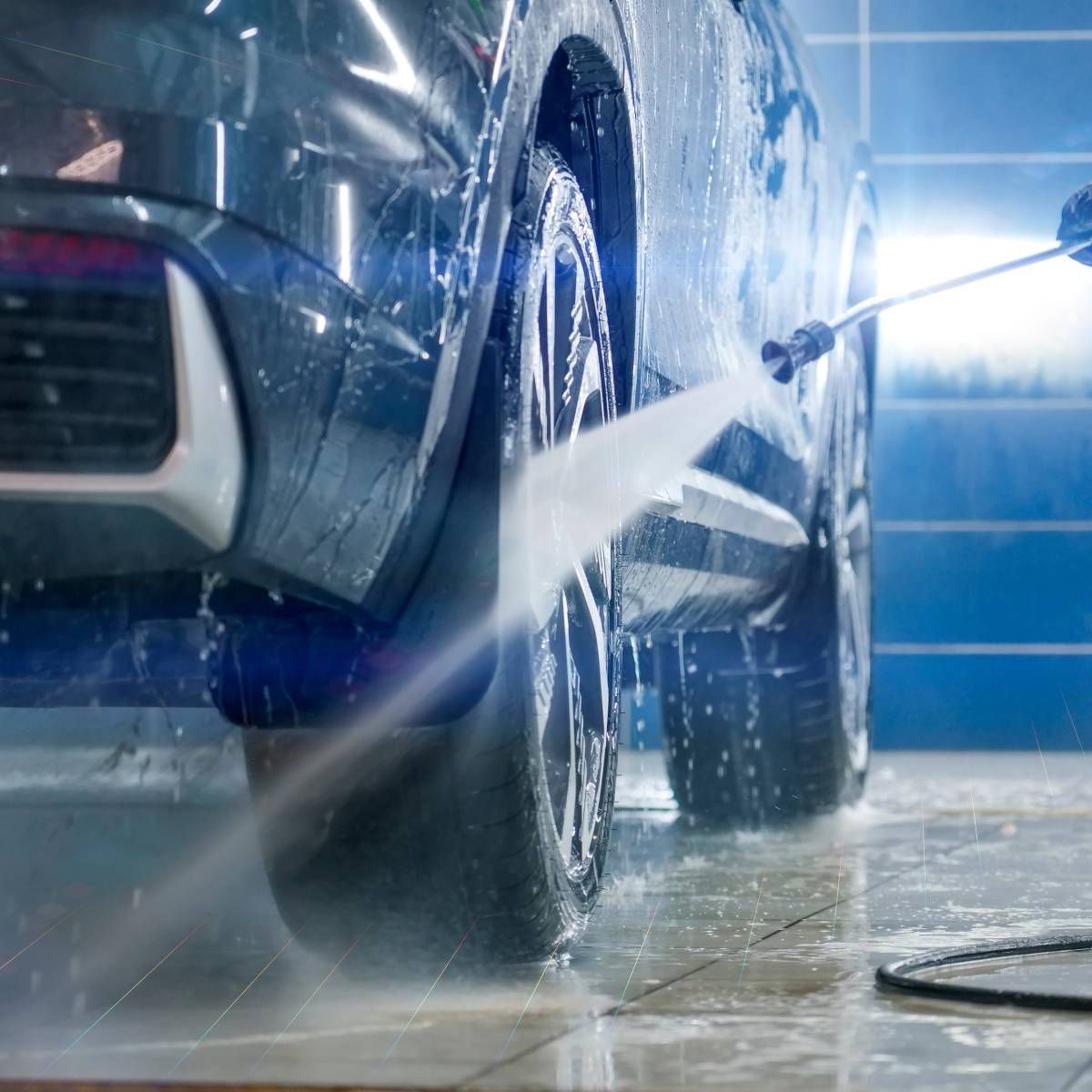 Car being washed with a high-pressure hose at a car wash, with water spraying.