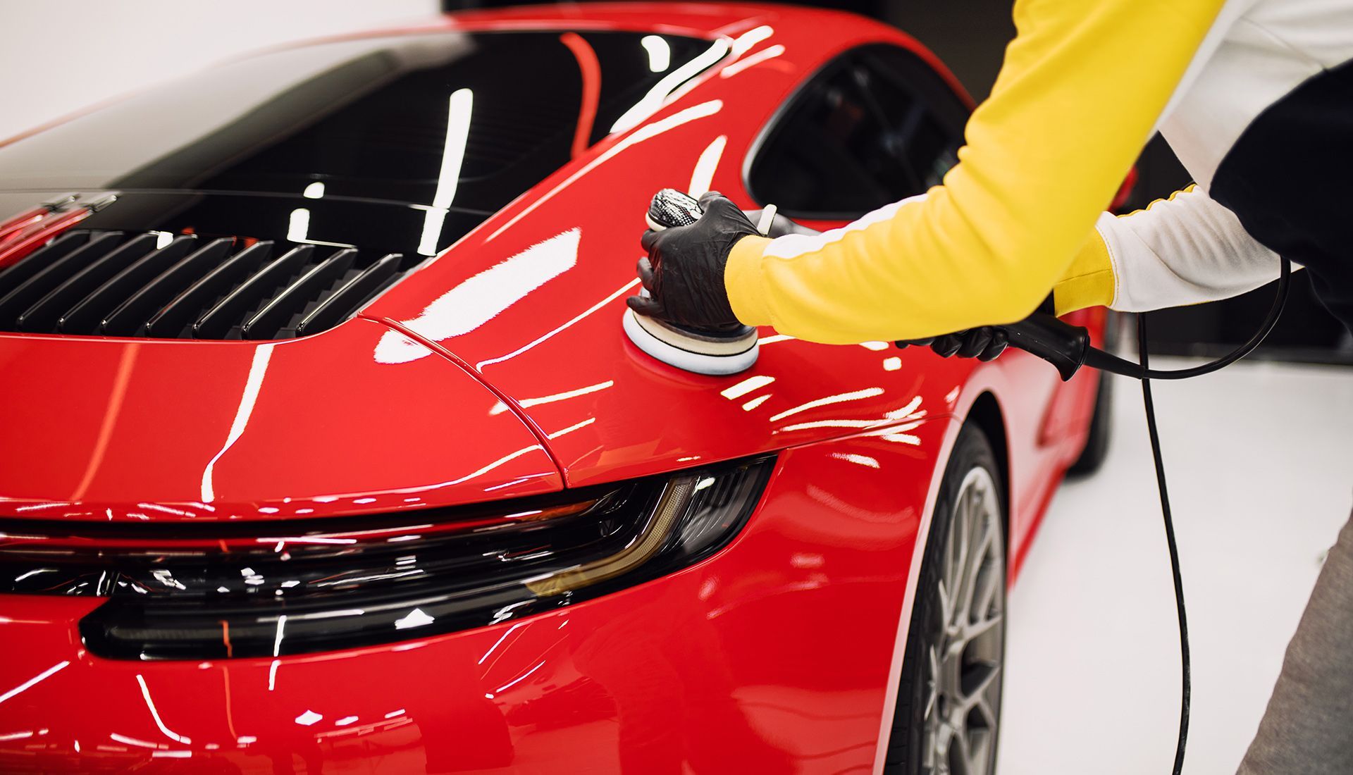 A person is polishing a red sports car with a machine.
