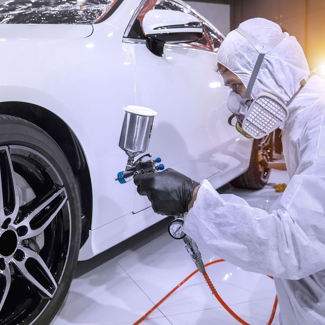 Person in protective suit spraying paint on a white car with black wheels.