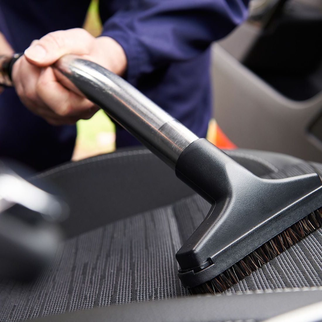 Person vacuuming car seat with a brush attachment.