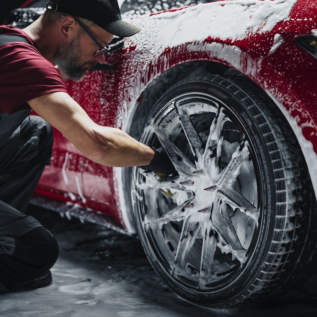 Man washing red car tire with foam in a garage.