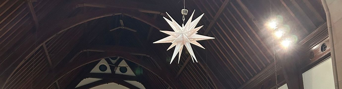 Two white stars are hanging from the ceiling of a church.