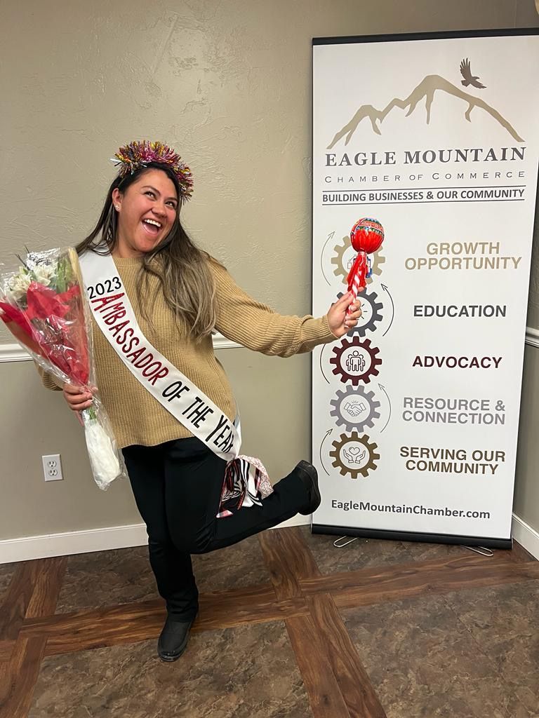 A woman is wearing a sash and holding a bouquet of flowers.