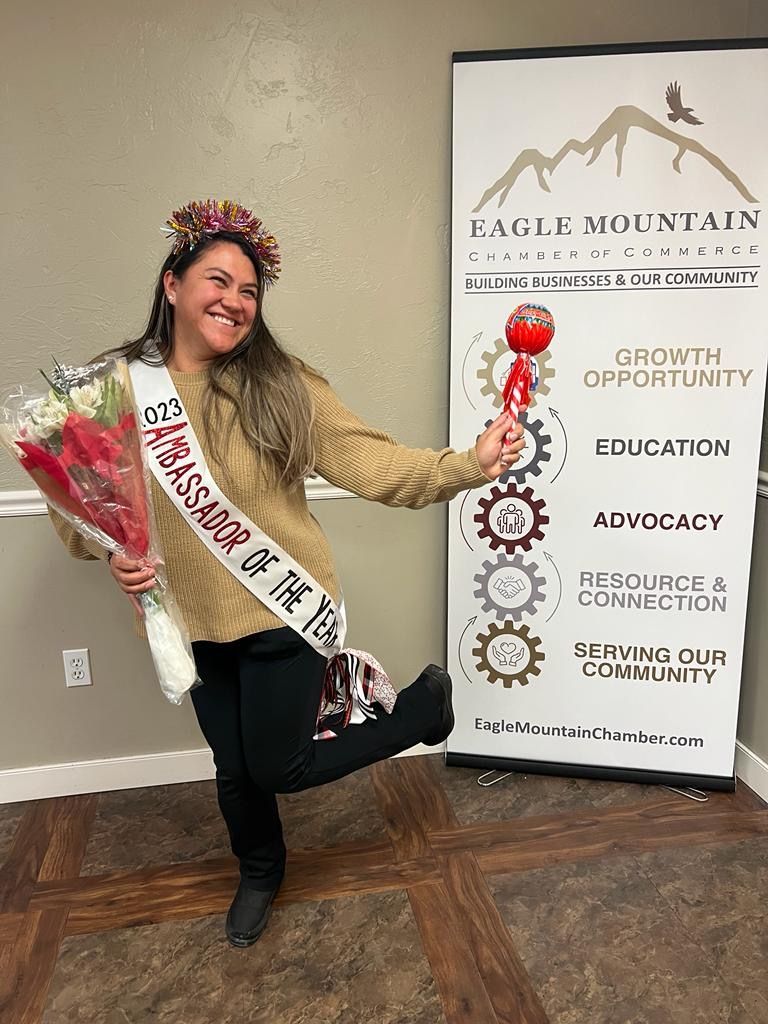 A woman is wearing a sash and holding a bouquet of flowers.